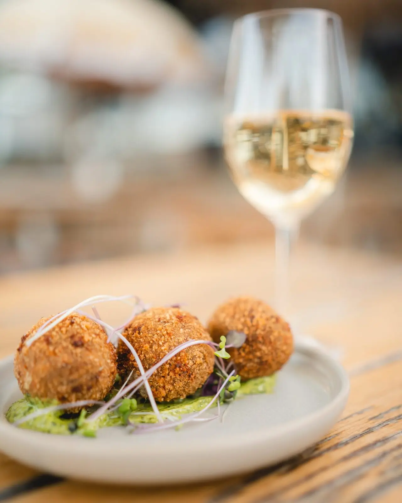 Three arancini on a plate beside a glass of sparkling wine