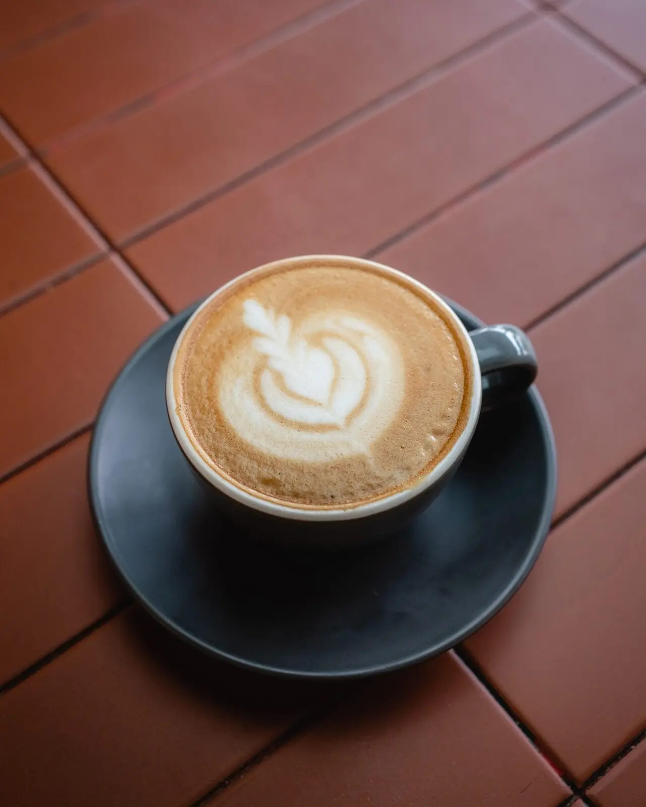 A latte in a black cup on terracotta tiles